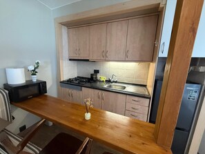 Eine kleine Küche mit Holzausstattung, einem Edelstahl-Spülbecken, einer Mikrowelle und einem Kühlschrank.