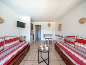 Ein Zimmer mit zwei gestreiften Sofas, einem kleinen Tisch mit Tassen, einem Fernseher und einer Küchenzeile im Hintergrund.