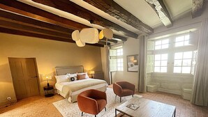 A bedroom with a bed, two armchairs, a coffee table, a fireplace, and a large window.
