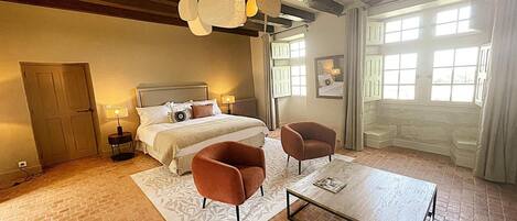 Un dormitorio con una cama, dos sillones, una mesita de centro, una chimenea y un ventanal grande.