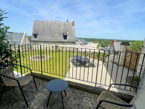 Un balcon donnant sur une cour, un bâtiment en pierre et un espace verdoyant.