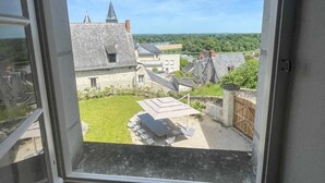 A view from a window overlooking a courtyard with a table and chairs, stone buildings, and a clear sky.