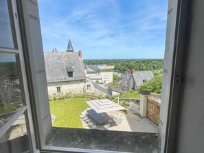 A view from a window overlooking a courtyard with a table and chairs, stone buildings, and a clear sky. - Charming cottage in Candes-St-Martin - 8 guests (Candes-Saint-Martin)