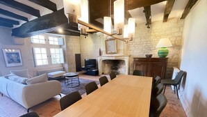 A room with a wooden dining table, sofas, a fireplace, and hanging light fixtures.