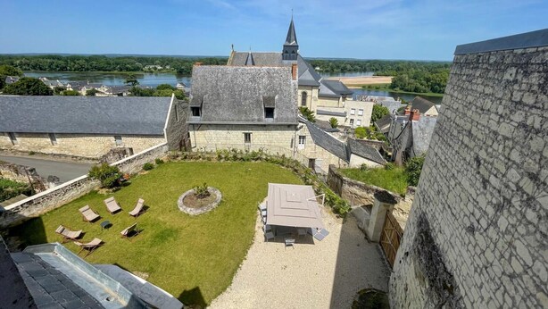 A courtyard with a lawn, lounge chairs, and a stone building with a tower.