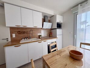 Eine moderne Küche mit weißen Schränken, einer Holzauskładung, einem Spülbecken, einem Herd und einem Esstisch mit Stühlen.