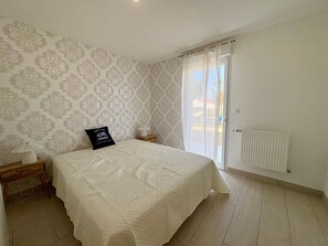 Ein Schlafzimmer mit einem Bett, einem Nachttisch, einer Lampe, einem Fenster mit Vorhängen und einer Heizung.
