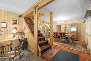 Eine Holztreppe mit Geländer, ein Essbereich mit Holzmöbeln und eine Küche mit Schränken und einem Kühlschrank.