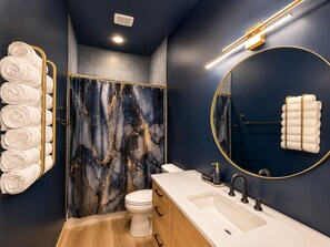 Une salle de bain moderne avec un mur de douche en marbre, des toilettes, un lavabo avec un meuble-vasque et des porte-serviettes.