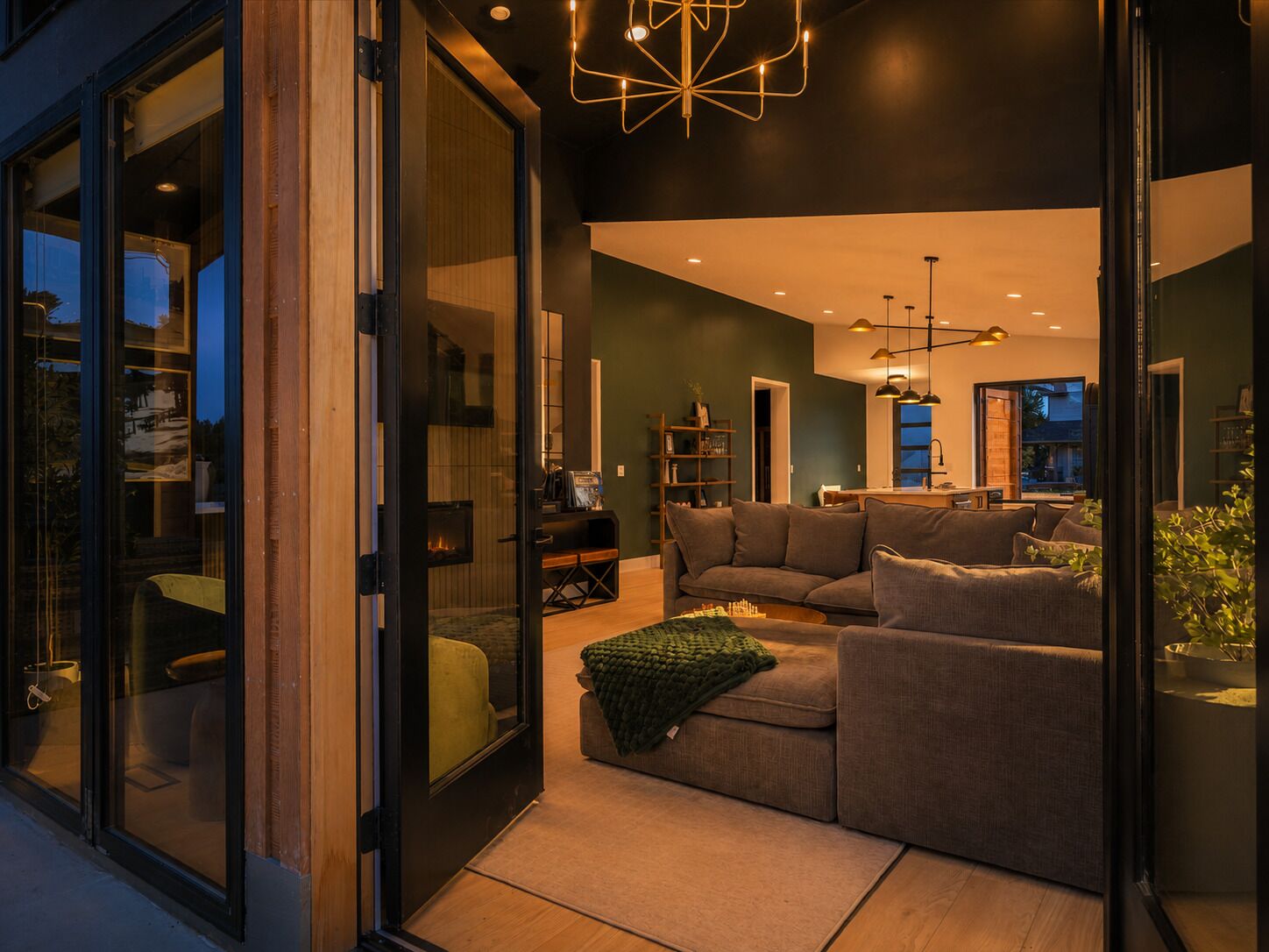 Una sala de estar moderna con un sofá modular, una chimenea y un comedor visible a través de puertas de cristal.