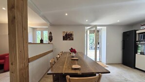 A dining area with a long wooden table, chairs, a vase with flowers, a clock, and a refrigerator. - Country house, private parking - 8 guests (Doissat)