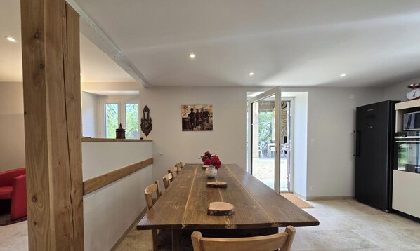 A dining area with a long wooden table, chairs, a vase with flowers, a clock, and a refrigerator. - Country house, private parking - 8 guests (Doissat)