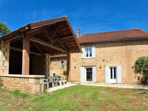 A stone house with a covered patio, a stone wall, and a small garden. - Country house, private parking - 8 guests (Doissat)
