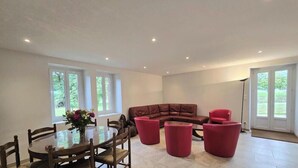 A spacious room with a dining table, chairs, a brown leather sofa, and red ottomans. - Country house, private parking - 8 guests (Doissat)