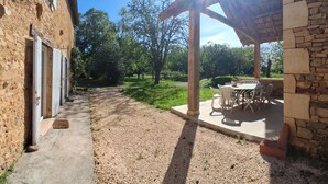 A courtyard with a stone building, a covered patio with outdoor furniture, and a gravel path. - Country house, private parking - 8 guests (Doissat)