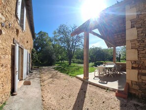 A courtyard with a stone building, a covered patio with outdoor furniture, and a gravel path. - Country house, private parking - 8 guests (Doissat)