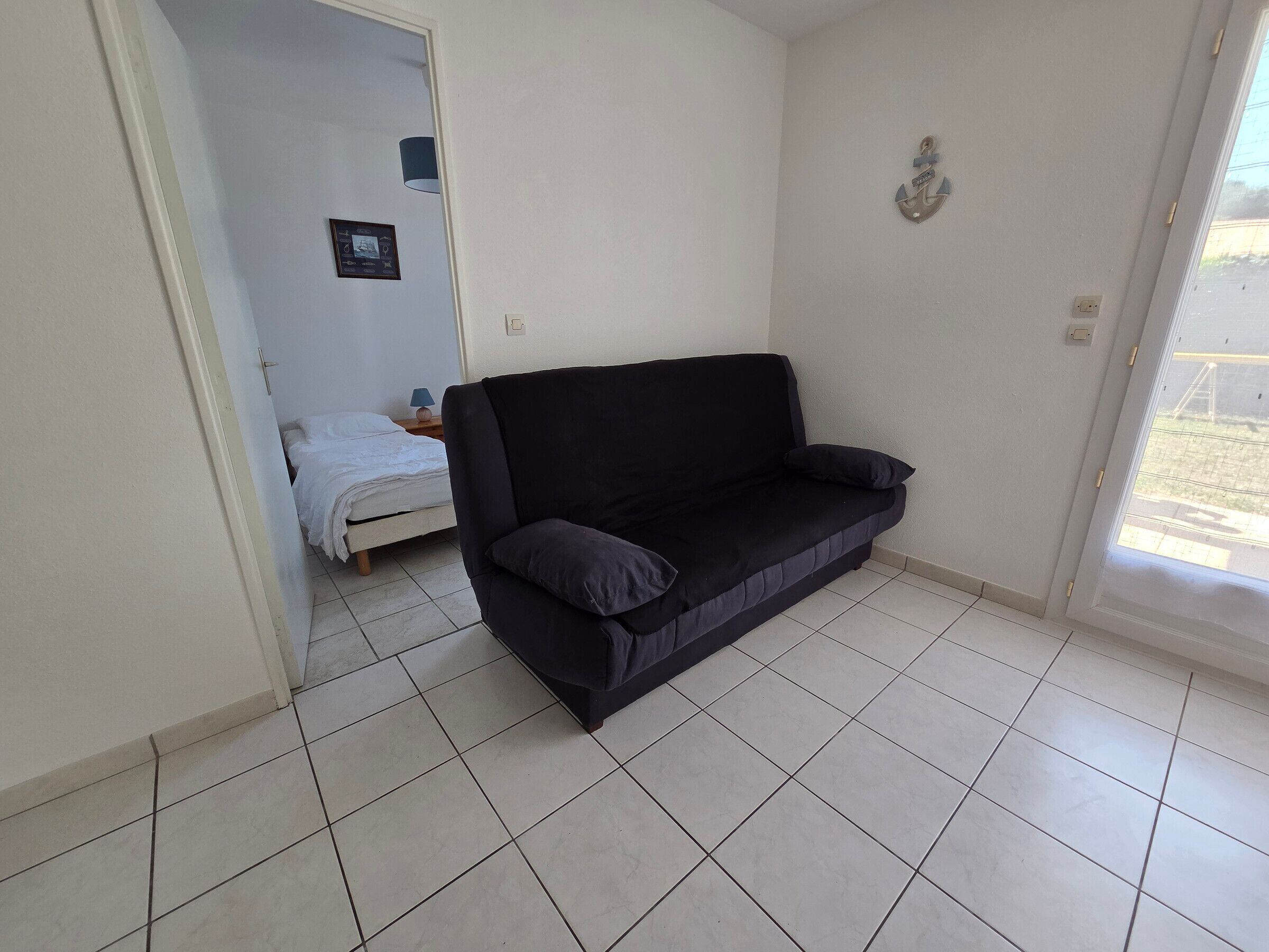 Une pièce avec un canapé noir, un lit avec une literie blanche, une petite table avec une lampe et un tableau accroché au mur.