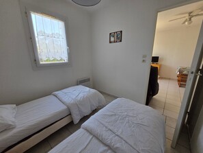 Eine kleine, einfache Unterkunft mit zwei Einzelbetten, einem Fenster mit Aussicht, einem Heizkörper, einem Tisch und einem Stuhl.