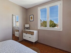 Ein Schlafzimmer mit Bett, Kommode, Spiegel, Fenster und einem gerahmten Bild an der Wand.