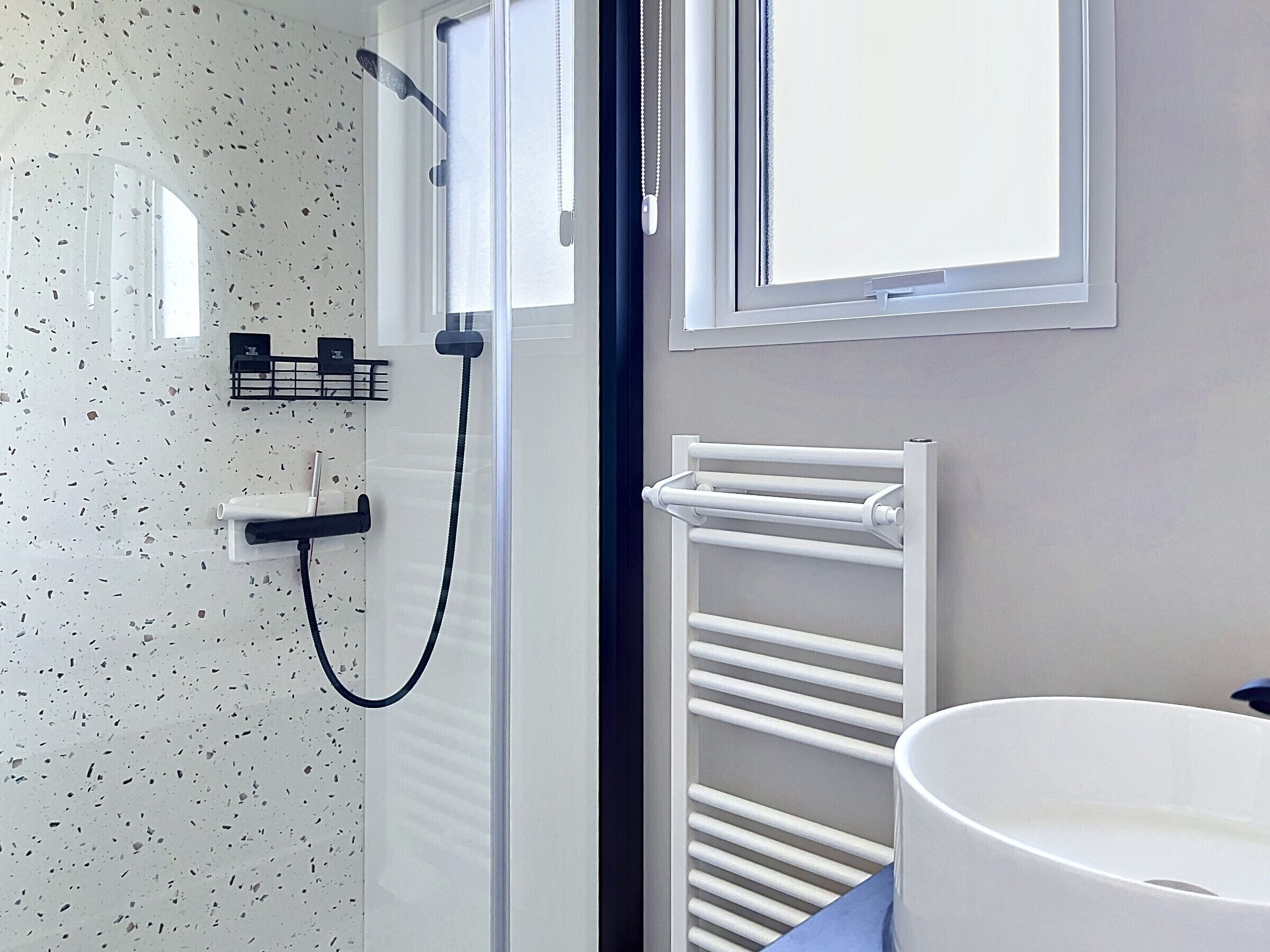Une salle de bain avec une douche, un porte-serviettes, un lavabo et une fenêtre.