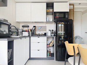 Une cuisine compacte avec des meubles blancs, un four à micro-ondes, un réfrigérateur noir et un coin repas comprenant une table et des chaises.