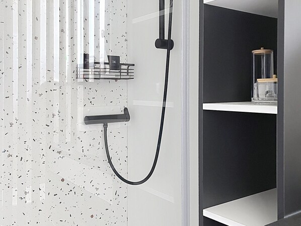 Une salle de bain avec une douche, une porte en verre et une étagère sur laquelle se trouve un récipient en verre.
