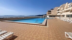 Une piscine sur le toit offrant une vue dégagée sur la mer, entourée de chaises longues et bordée d’un immeuble doté de balcons.