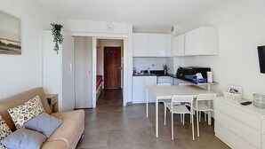 Un espace de vie compact comprenant un coin cuisine, un coin repas et un canapé avec des coussins.