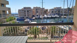 Un balcon avec une table et des chaises, donnant sur une marina où l’on peut admirer des bateaux et des bâtiments.