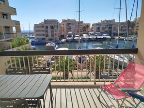 Ein Balkon mit Tisch und Stühlen, Blick auf einen Yachthafen mit Booten und Gebäuden.