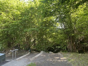 Un chemin pavé mène à une zone boisée, avec des garde-corps métalliques sur le côté gauche.