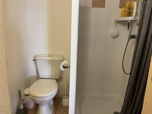Een badkamer met een toilet, een douche en een toiletborstel.