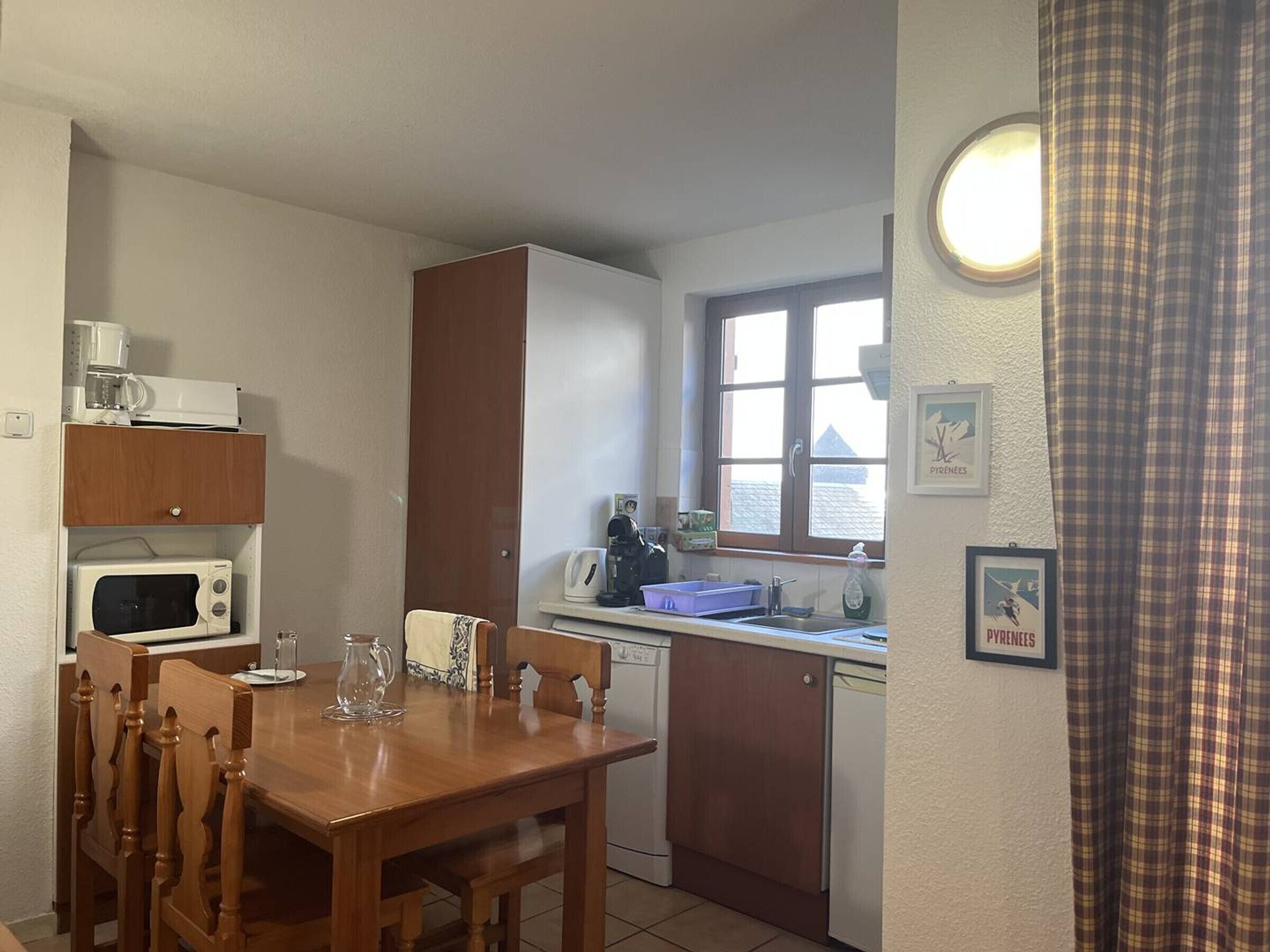 Eine kompakte Küche mit Esstisch, Stühlen, einer Mikrowelle, einer Kaffeemaschine und einem Fenster mit Vorhängen.