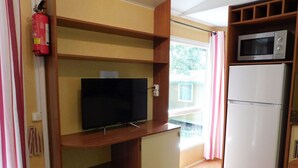 Pieni, käytännöllinen keittiönurkkaus, jossa on mikroaaltouuni, jääkaappi, litteänäyttöinen televisio puuhyllyllä ja palosammutin.