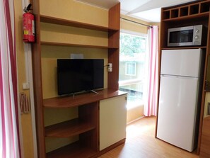 Eine kompakte Küchenzeile mit Mikrowelle, Kühlschrank, Flachbildfernseher auf einer Holzablage und einem Feuerlöscher.