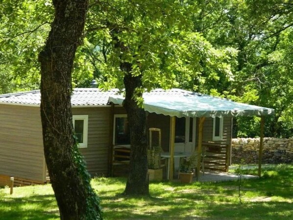A small, single-story cabin with a porch, surrounded by trees and a stone wall. - Mobile home, pets allowed - 5 guests (Vesseaux)