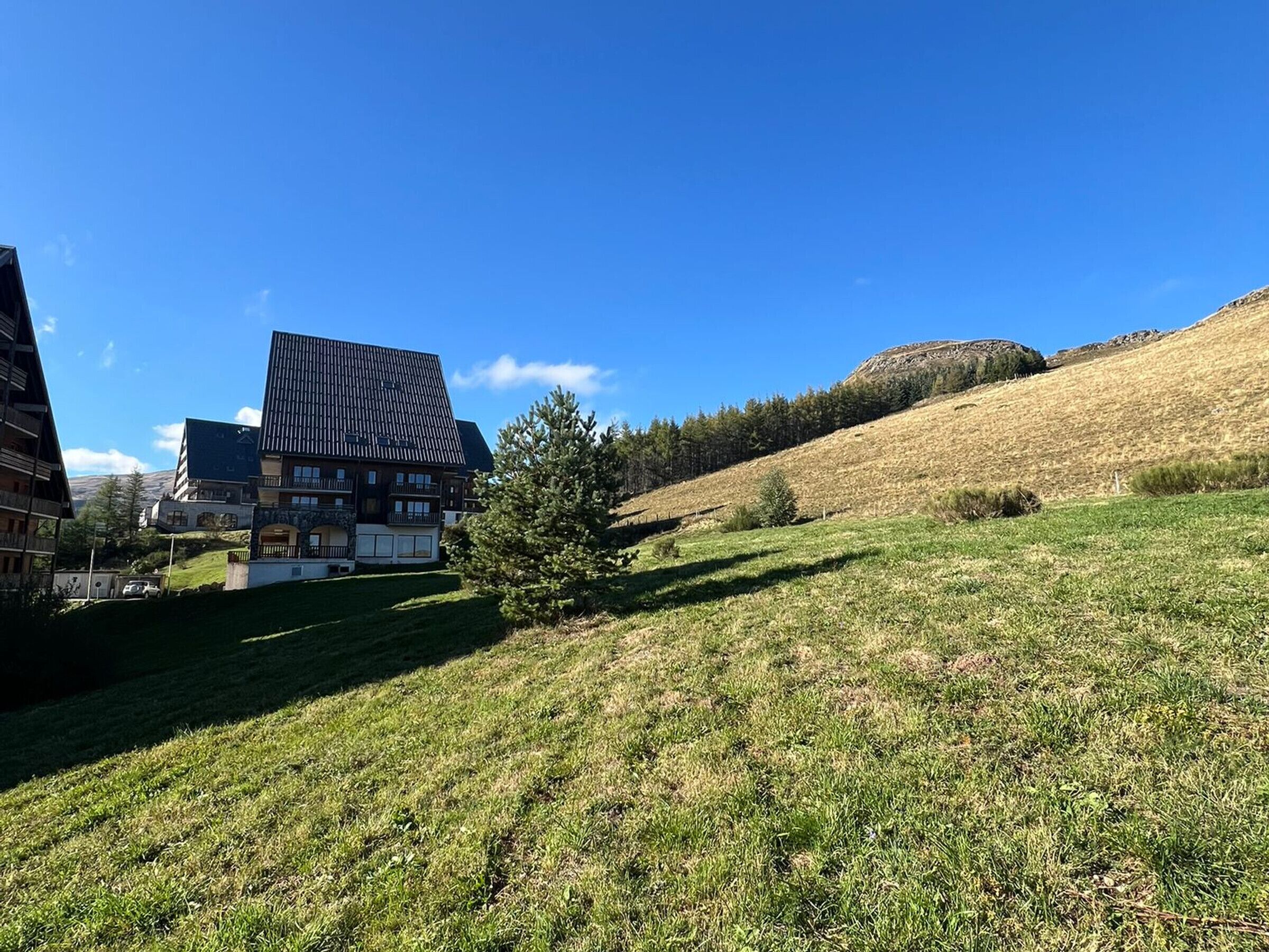Ein modernes Gebäude mit geneigtem Dach, einem grasbewachsen Hügel und einem Berg im Hintergrund.
