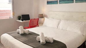 Une chambre d’hôtel avec un lit, un bureau avec un ordinateur portable, une chaise rouge et des œuvres d’art accrochées au mur.
