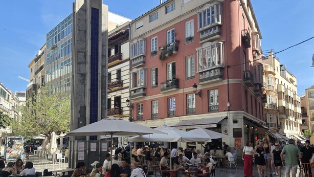 Un café en plein air, avec des tables et des parasols, entouré de bâtiments historiques dotés de balcons et de fenêtres.
