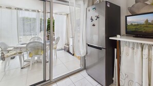 A modern kitchen with a refrigerator, a television, and a dining area with chairs and a table. - Studio with pool, parking - 4 guests (Marseillan-Plage)