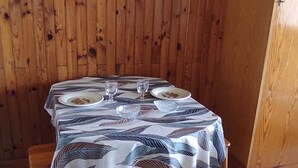 Ein Esstisch mit einer Tischdecke mit Blattmuster, zwei Tellern und zwei Weingläsern, vor einer Holzwand.