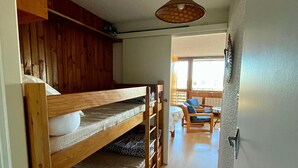 Ein Schlafraum mit Etagenbetten, einem Holzkopfteil, einem Tisch mit Stühlen und Blick ins Freie.
