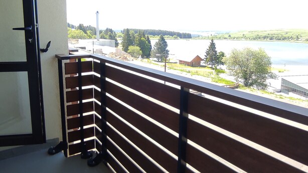 Ein Balkon mit Blick auf einen See, Bäume und ein Gebäude in der Ferne.