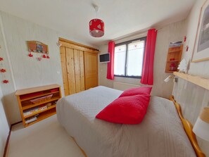 A bedroom with a bed, wooden wardrobe, television, and a window with curtains.