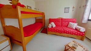 Una cama individual superpuesta con adorno de reno, un sofá rojo con estampados blancos y una mesita de madera.