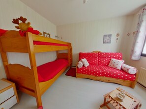 Una cama individual superpuesta con adorno de reno, un sofá rojo con estampados blancos y una mesita de madera.