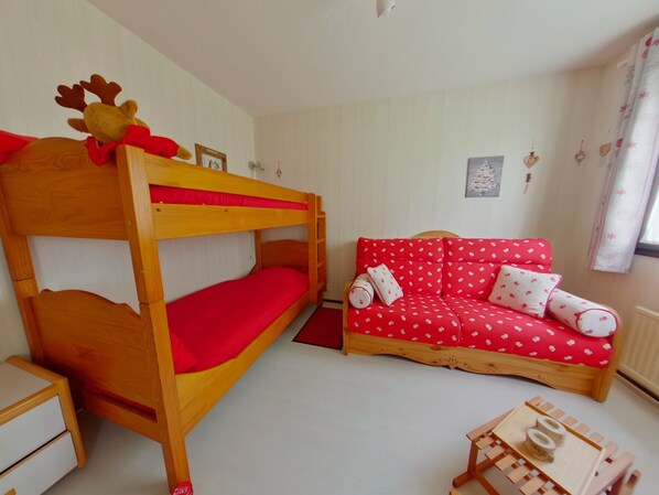 A bunk bed with a reindeer decoration, a red sofa with white patterns, and a wooden side table.