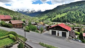 A mountain village with traditional wooden houses, a road, and a view of snow-capped mountains. - Pleasant duplex with view - 6 guests (Le Grand-Bornand)