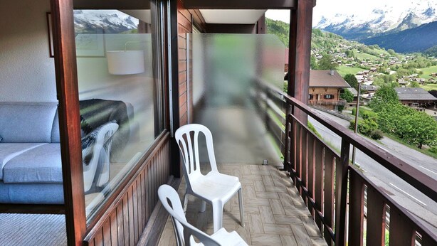 A balcony with a view of a mountain landscape, a sofa, and two white chairs. - Pleasant duplex with view - 6 guests (Le Grand-Bornand)