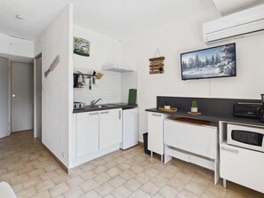 Eine kompakte Küche mit weißen Schränken, einer Mikrowelle, einem Spülbecken und einem kleinen Fenster.